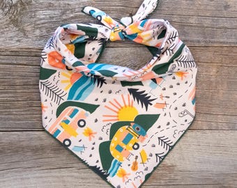 May include: A white bandana with a green border featuring a colourful pattern of camping scenes, including a yellow sun, blue water, green trees, and pink and yellow camper vans.