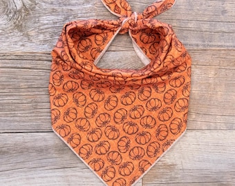 Peut inclure: Bandana pour chien orange et marron avec un motif de citrouilles. Le bandana est noué en haut et présente un motif répété de citrouilles. Il a une bordure blanche. Le tissu semble doux.