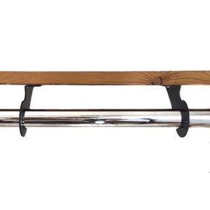 May include: A wooden shelf with a polished chrome bar below. The shelf is supported by black metal brackets. The wood has a natural grain and warm brown color. The chrome bar reflects light.