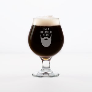 May include: A clear glass beer goblet with a dark brown beer inside. The glass has the text "I'm a Bearded Nerd" with a beard graphic etched into the glass.