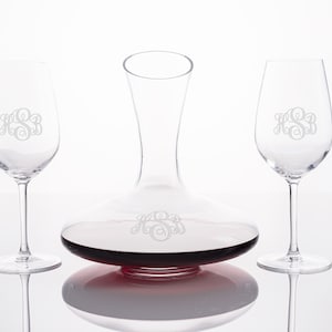 May include: A set of two clear glass wine glasses and a clear glass decanter, all engraved with the monogram "HSB". The decanter is filled with red wine.