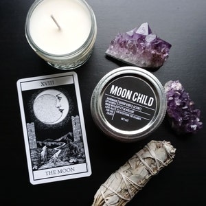 Peut inclure: Une carte de tarot noir et blanc avec l'image de la lune et le texte "XVIII THE MOON". Une bougie blanche dans un bocal en verre, un bocal en argent avec une &eacute;tiquette noire qui indique "MOON CHILD HANDMADE SOY CANDLE | GOOD VIBES SCENT! | MADE WITH | BYETTA AIRLENE | LOVE, JUST | FOR YOU | CREATED FROM THE COSMOS | NET 4 OZ", deux cristaux d'am&eacute;thyste et un fagot de sauge blanche sont &eacute;galement pr&eacute;sents sur l'image.