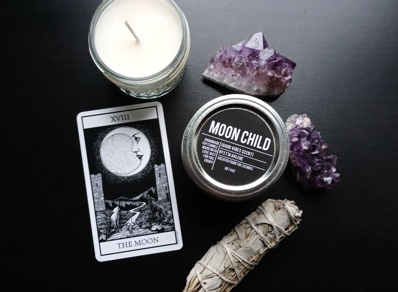 Peut inclure: Une carte de tarot noir et blanc avec l'image de la lune et le texte "XVIII THE MOON". Une bougie blanche dans un bocal en verre, un bocal en argent avec une &eacute;tiquette noire qui indique "MOON CHILD HANDMADE SOY CANDLE | GOOD VIBES SCENT! | MADE WITH | BYETTA AIRLENE | LOVE, JUST | FOR YOU | CREATED FROM THE COSMOS | NET 4 OZ", deux cristaux d'am&eacute;thyste et un fagot de sauge blanche sont &eacute;galement pr&eacute;sents sur l'image.