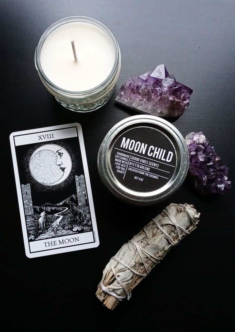 Peut inclure: Une carte de tarot noir et blanc repr&eacute;sentant La Lune (XVIII) avec un croissant de lune, deux tours et un loup. Un b&acirc;tonnet de sauge blanche, un cristal d'am&eacute;thyste violet, une bougie dans un bocal en verre et un bocal de bougie &eacute;tiquet&eacute; "Moon Child" sont &eacute;galement pr&eacute;sents sur l'image.