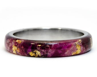 Puede incluir: Un anillo de metal con una incrustación de resina morada y dorada. El anillo es liso y pulido.
