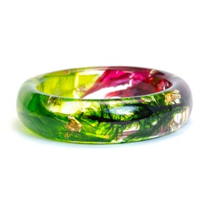 May include: A vibrant resin ring with a botanical design. The ring features a clear band with embedded green, red, and gold leaf accents. The ring is a unique piece of jewelry.