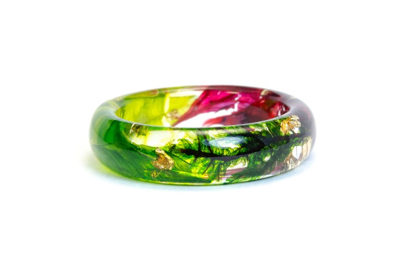 May include: A vibrant resin ring with a botanical design. The ring features a clear band with embedded green, red, and gold leaf accents. The ring is a unique piece of jewelry.