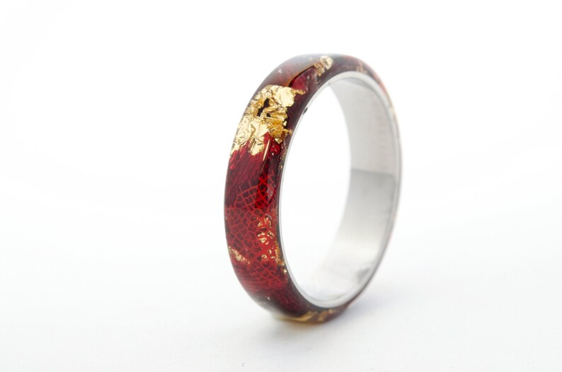 Puede incluir: Un anillo rojo y dorado con una banda plateada. El anillo est&aacute; hecho de resina y tiene un dise&ntilde;o &uacute;nico con escamas doradas incrustadas en la resina roja.