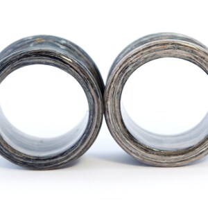 May include: A pair of wooden ear gauges with a black and white wood grain pattern. The gauges are round and have a smooth, polished finish.