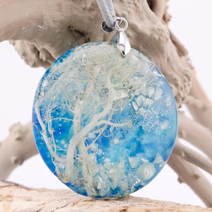 May include: Round blue resin pendant with a white tree-like design and silver bail. The pendant is filled with glitter and small white pieces.