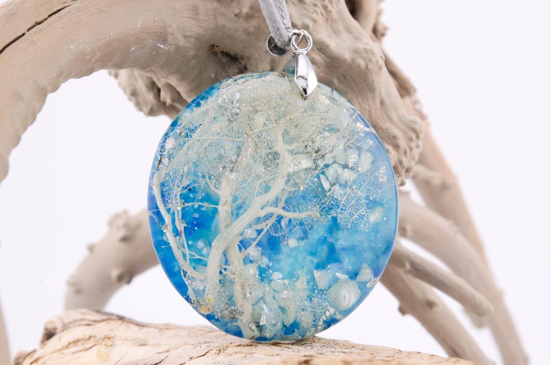May include: Round blue resin pendant with a white tree-like design and silver bail. The pendant is filled with glitter and small white pieces.