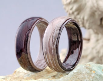 May include: Two wooden rings with a unique marbled pattern. One ring is a dark brown with white streaks, and the other is a light brown with dark brown streaks.