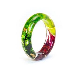 May include: A colorful resin ring with a nature-inspired design. The ring features a gradient of green, yellow, and red hues, with gold leaf accents. The ring is a unique piece of jewelry.