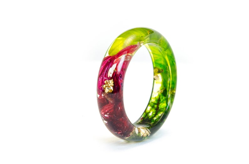 May include: A clear resin ring with embedded flowers and gold flakes. The ring features a vibrant mix of colors, including deep red, green, and gold. The ring is a unique piece of jewelry.
