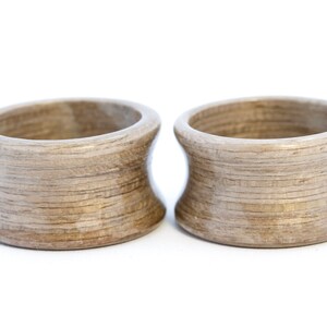 May include: Two wooden rings with a light brown color and a wood grain pattern. The rings are slightly flared at the top and bottom.