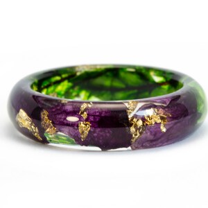 K&ouml;nnte beinhalten: Handgefertigter Ring mit transparentem Harzband. Der Ring zeigt eine Mischung aus lila und gr&uuml;nen floralen Elementen, akzentuiert mit Blattgoldflocken. Ein einzigartiges Schmuckst&uuml;ck.