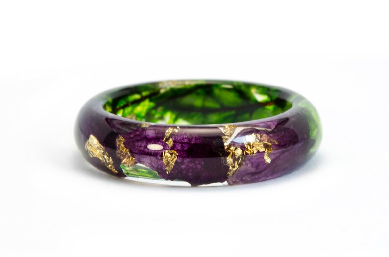 K&ouml;nnte beinhalten: Handgefertigter Ring mit transparentem Harzband. Der Ring zeigt eine Mischung aus lila und gr&uuml;nen floralen Elementen, akzentuiert mit Blattgoldflocken. Ein einzigartiges Schmuckst&uuml;ck.