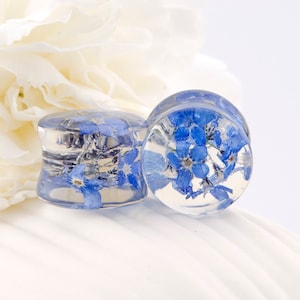 May include: Two clear glass ear gauges with blue forget-me-not flowers pressed inside. The gauges are round and have a smooth, polished finish.