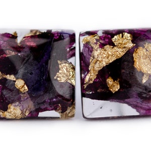 May include: A pair of square resin earrings with purple and gold flower petals and gold leaf accents.