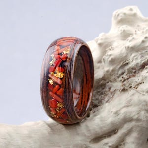 Peut inclure: Une bague en bois avec une bande de corail rouge et des paillettes d'or incrustées dans de la résine transparente.