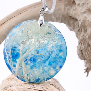 May include: A round blue and white resin pendant with a white tree design. The pendant is hanging from a silver chain.