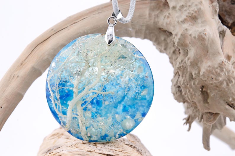 May include: A round blue and white resin pendant with a white tree design. The pendant is hanging from a silver chain.