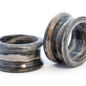 May include: Two wooden rings with a black, white, and brown striped pattern. The rings are made of layered wood and have a smooth, polished finish.