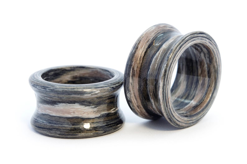May include: Two wooden rings with a black, white, and brown striped pattern. The rings are made of layered wood and have a smooth, polished finish.