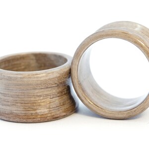 May include: Two wooden ear gauges, one is a flared style and the other is a simple ring style. Both are a light brown color with a wood grain pattern.