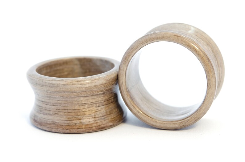 May include: Two wooden ear gauges, one is a flared style and the other is a simple ring style. Both are a light brown color with a wood grain pattern.