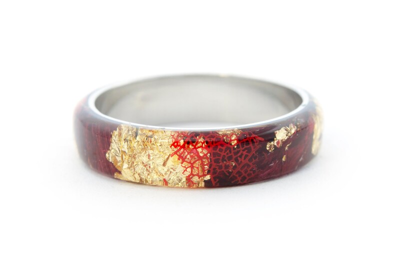 Puede incluir: Un anillo de banda de plata con una incrustaci&oacute;n de resina roja y dorada. La resina tiene un aspecto texturizado, marmoleado con escamas doradas.