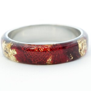 Puede incluir: Un anillo de plata con una incrustaci&oacute;n de resina roja y dorada. La resina tiene un patr&oacute;n texturizado de encaje.