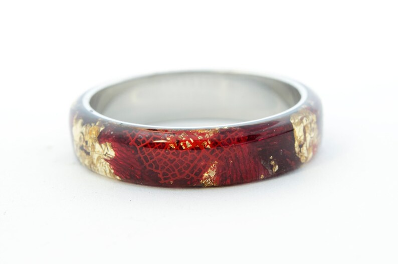 Puede incluir: Un anillo de plata con una incrustaci&oacute;n de resina roja y dorada. La resina tiene un patr&oacute;n texturizado de encaje.