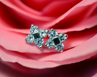 Puede incluir: Un par de pendientes de plata con un diseño de cuatro puntas, cada punta engastada con un diamante transparente. Los pendientes están sobre un pétalo de rosa rosa.