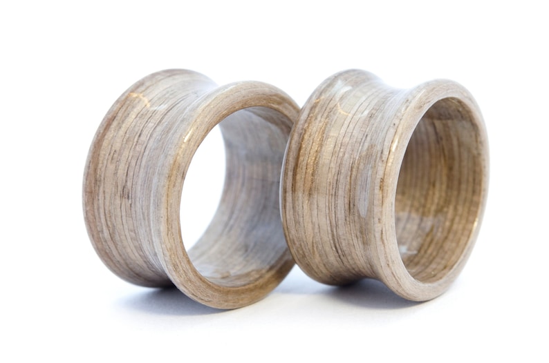May include: Two wooden ear gauges, one on top of the other, with a light brown wood grain pattern.