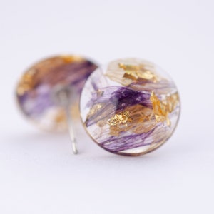 Op de afbeelding: Een paar ronde hars oorbellen met paarse en gouden accenten. De oorbellen zijn doorschijnend en hebben een delicate, etherische uitstraling.