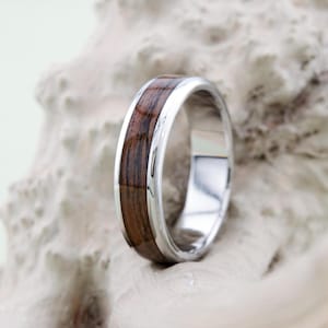 Op de afbeelding: Een zilveren band met een donkerbruine houten inlay. De ring ligt op een witte achtergrond.