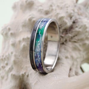 Puede incluir: Un anillo de plata con una incrustación negra, verde, azul y blanca. La incrustación tiene una textura brillante y brillante.