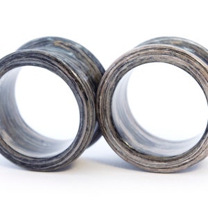 May include: A pair of black and grey wooden ear gauges. The gauges are round and have a smooth, polished finish.