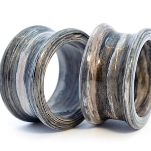 May include: Two wooden ear gauges with a layered, striped pattern in shades of gray, brown, and white. The gauges have a smooth, polished finish.