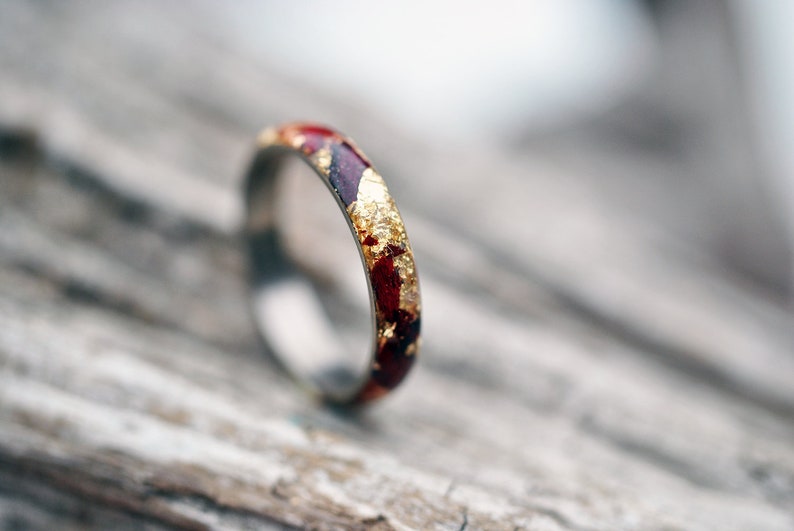 Puede incluir: Un anillo de banda delgado de oro y rojo con escamas de oro incrustadas en la resina roja.