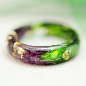 K&ouml;nnte beinhalten: Handgefertigter Harzring mit einer Kombination aus lila und gr&uuml;nen Farbt&ouml;nen, verziert mit Blattgoldflocken. Der Ring zeigt ein einzigartiges Blumendesign, das jedem Outfit einen Hauch von nat&uuml;rlicher Eleganz verleiht. Ein Schmuckst&uuml;ck.