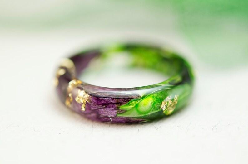K&ouml;nnte beinhalten: Handgefertigter Harzring mit einer Kombination aus lila und gr&uuml;nen Farbt&ouml;nen, verziert mit Blattgoldflocken. Der Ring zeigt ein einzigartiges Blumendesign, das jedem Outfit einen Hauch von nat&uuml;rlicher Eleganz verleiht. Ein Schmuckst&uuml;ck.