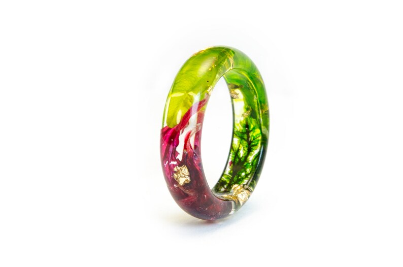 May include: A clear resin ring with embedded botanical elements. The ring features a gradient of colors, transitioning from deep burgundy to vibrant green. Gold leaf flakes add sparkle.