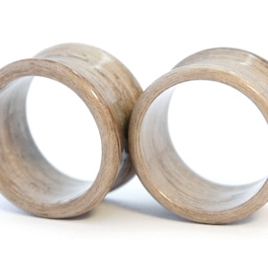 May include: A pair of wooden ear gauges, one on top of the other, with a light brown wood grain pattern.