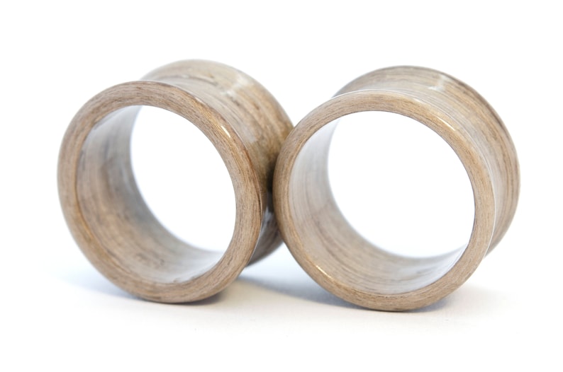 May include: A pair of wooden ear gauges, one on top of the other, with a light brown wood grain pattern.