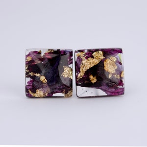 May include: A pair of square resin earrings with purple and gold flower petals and gold leaf accents.