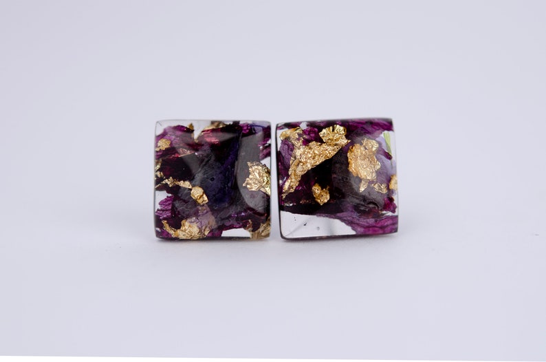 May include: A pair of square resin earrings with purple and gold flower petals and gold leaf accents.