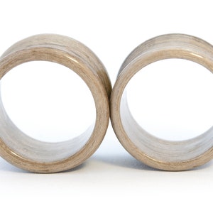 May include: A pair of wooden ear gauges, each with a light brown color and a smooth, polished finish.