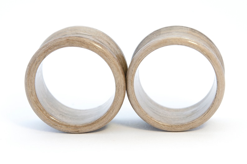 May include: A pair of wooden ear gauges, each with a light brown color and a smooth, polished finish.
